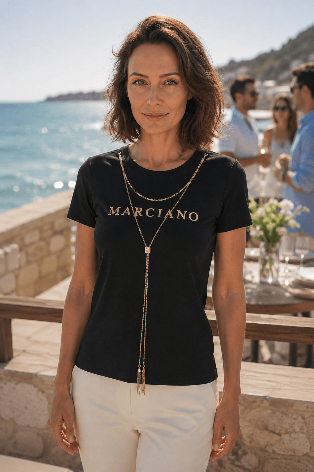 Model in een zwart Marciano by Guess logo-T-shirt met goudkleurige ketting op een evenement buiten.