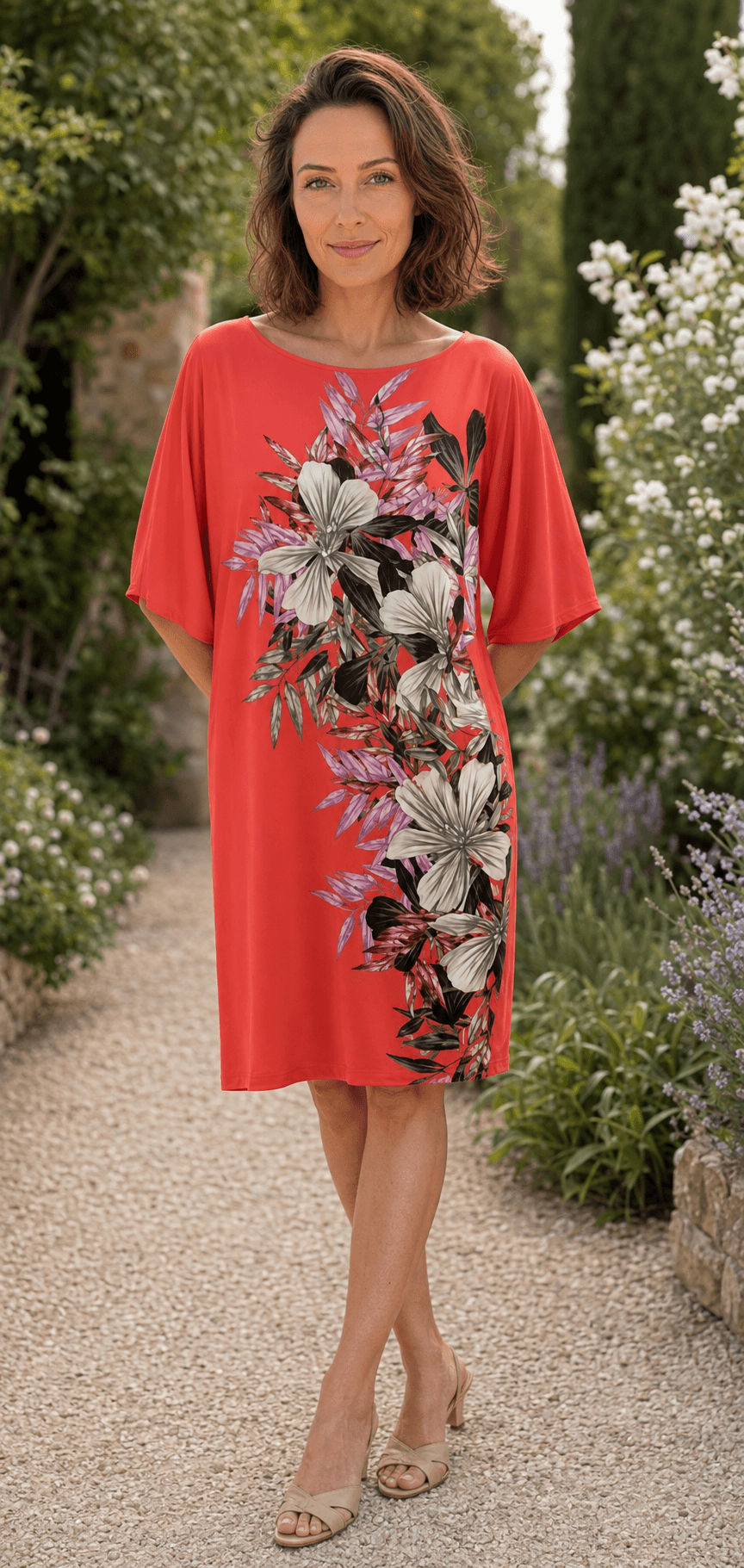 Model in een koraalkleurige Marciano by Guess rechte jurk met bloemenprint in een tuin.