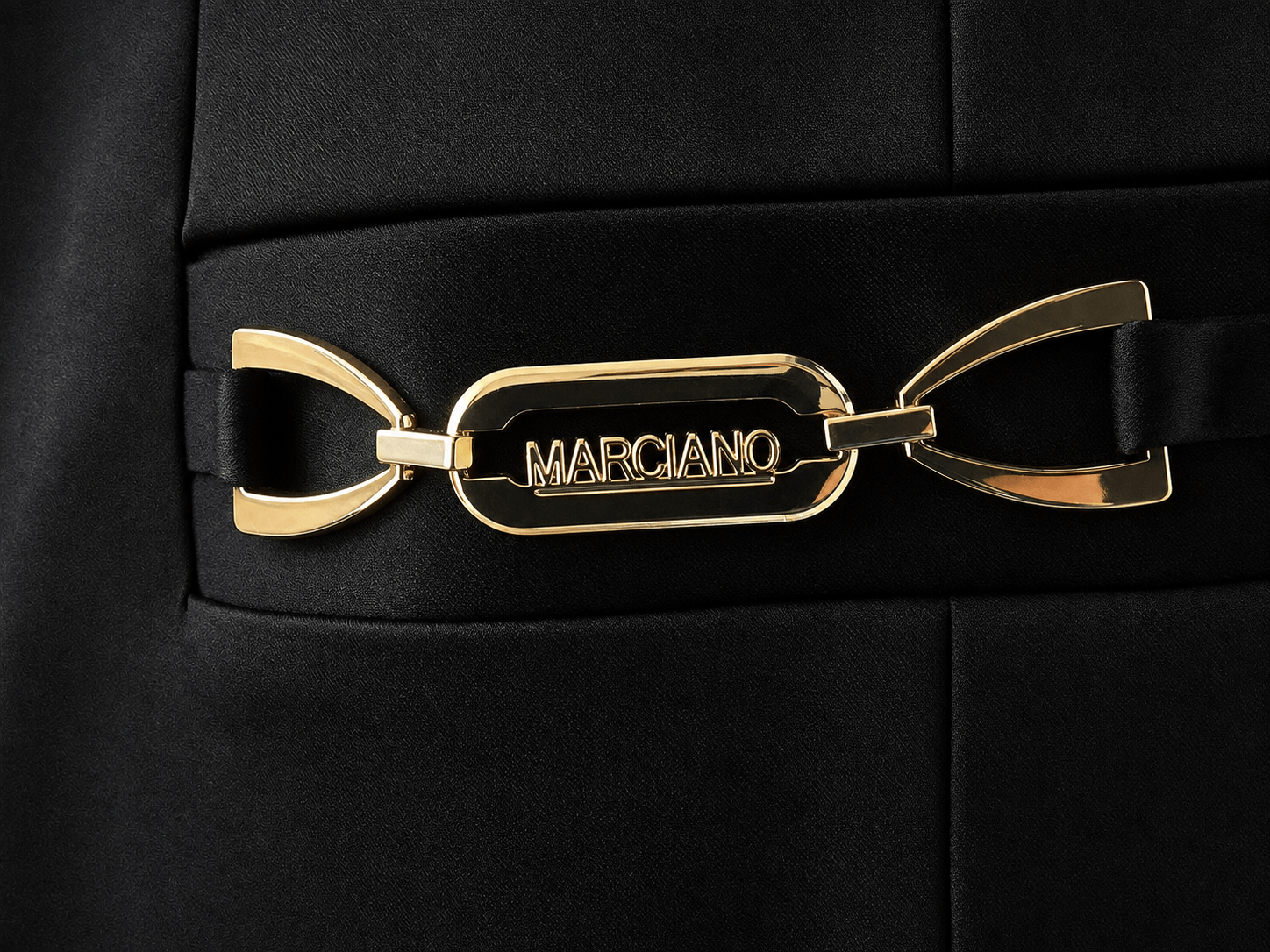 Detail van het goudkleurige logo op een zwarte Marciano by Guess blazer met satijnglans.